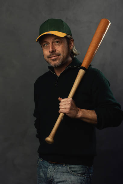 homem loiro sorridente com boné de beisebol e bastão em um suéter de lã verde escuro. - men baseball baseball cap baseball bat - fotografias e filmes do acervo