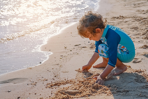 Baby boy playing with sand at sea. Child on vacation in summer at the beach on vacations