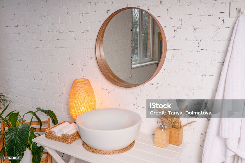 Large round mirror above the sink in a stylish light bathroom interior. Large round mirror above the sink in a stylish light bathroom interior. Lamp, a set of towels, indoor green plants. Nautical Vessel Stock Photo