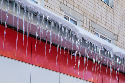 Lots of icicles hang from the roof. In the background is a brick wall of a residential building with windows.