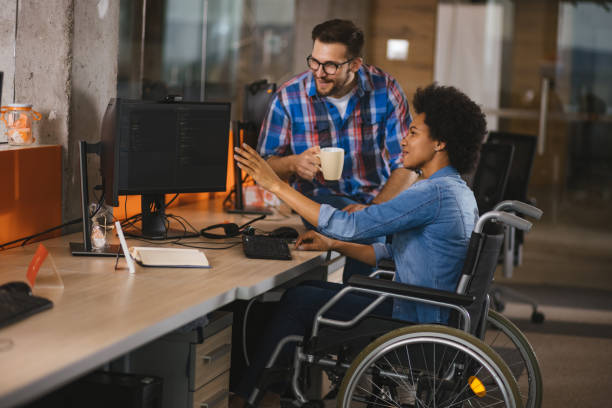 programador informático discapacitado sentado en silla de ruedas en el lugar de trabajo y colaborando con un colega - physical impairment wheelchair disabled accessibility fotografías e imágenes de stock