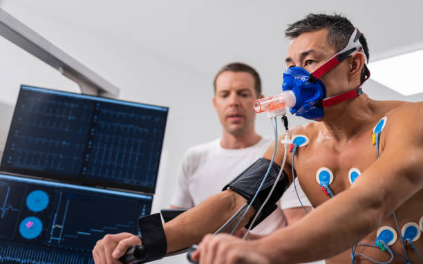 Male Athlete Performing ECG And VO2 Test On Indoor Bicycle Young adult man having a VO2 test with a VO2 mask on his face, electrocardiogram pads attached, computer recording, indoor bicycle. cardio pulmonary stock pictures, royalty-free photos & images