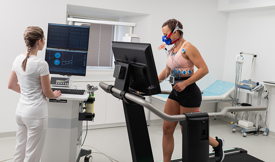 Female athlete having a VO2 test with VO2 mask on face, electrocartiogram pads attached, treadmill.