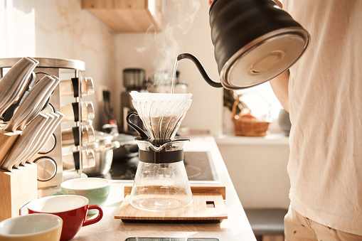 Cozy atmosphere. Close up view of the man preparing filter coffee for himself and his boyfriend while standing at the kitchen with teapot at his hands. Stock photo
