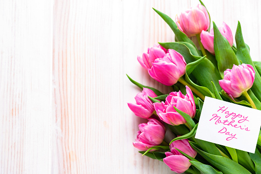Overhead view of a pink tulips bouquet and a greeting card with the text 