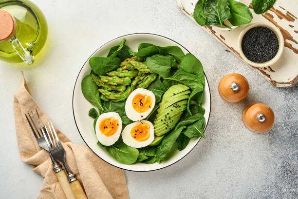 istock Fresh vegetable salad with avocado, asparagus, crumpled eggs with black sesame seeds and spinach on plate on light slate, stone or concrete background. Balanced lunch in bowl. Top view. Mock up. 1312654976