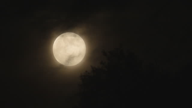 Full moon moves through the night sky, accompanied by small clouds.