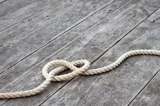 single loose knot of light coloured rope along bottom of frame on rustic wood background with copy space