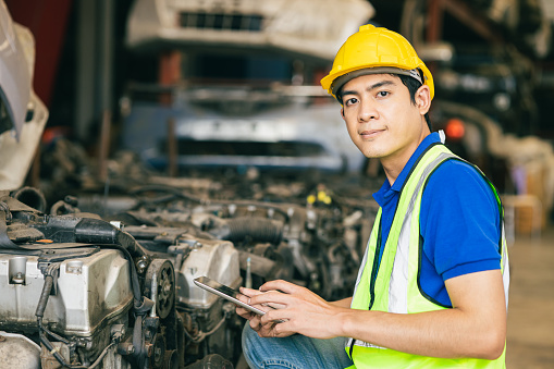 Asian Male Engineer Worker Working usign tablet to check old used Car Engine.