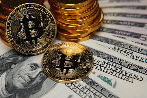 London, UK - 04 15 2021: Bitcoin coins cryptocurrency on US dollar banknotes background.