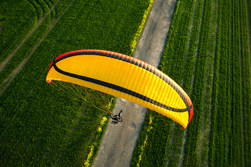 Sporting adventure: Paramotor or motorized parachute flying over a small road in the middle of a field at sunset