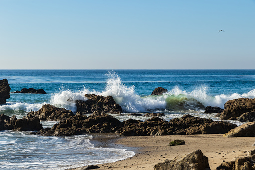 Wave breaking on rocks at Leo Carrillo State Beach, near Malibu, California. Blue Pacific ocean beyond; Seagull flying in sky.