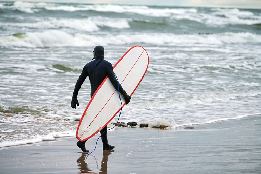 Male surfer in swim suit walking along sea with surfboard