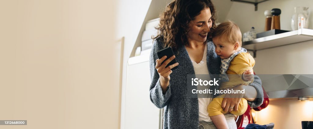 Woman on maternity leave spending time with her baby Smiling woman carrying her baby at home. Woman on maternity leave spending time with her baby. Smart Phone Stock Photo