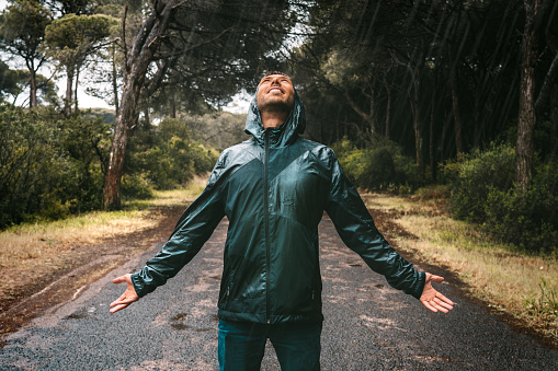 Young wet smiling man in drenched jacket with a hood enjoying rain. Man in raincoat stood in heavy rain. Bad autumn wether. High quality photo