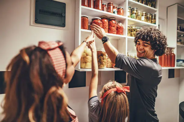 A happy family takes jars with pickled vegetables from the pantry shelf.