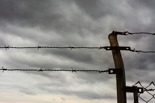 Two rows of barbed wire and a fence post, with storm clouds in the background. Immigration, escape or freedom concept.