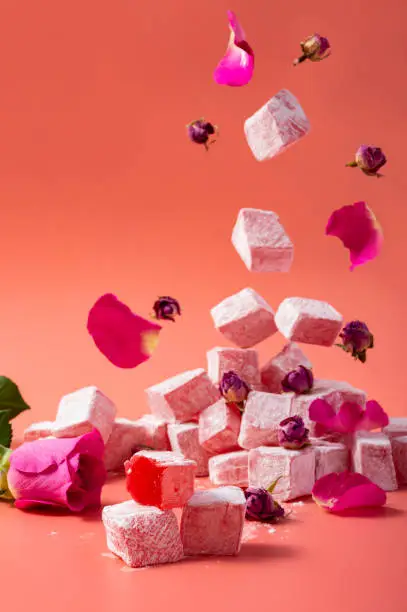 Levitating rose flavoured pink Turkish delight with flower petals and dry rosebuds on pink background