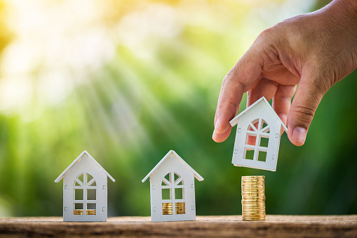 Man hand hold a wooden home model put on the stack coin with growing in the public park, Savings money for buy house and loan to business investment for real estate concept.
