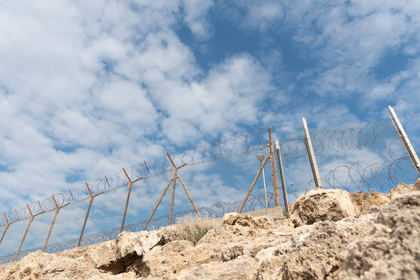 istock Security fence with barbed wire against a blue cloudy sky 1312682524