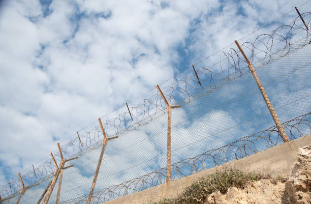 istock Security fence with barbed wire against a blue cloudy sky 1312682544