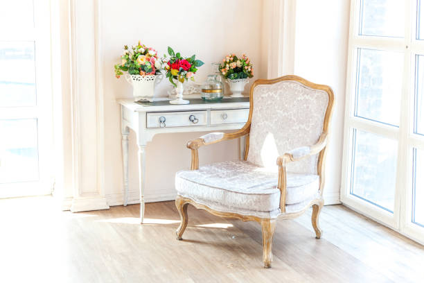 Beautiful luxury classic white bright clean interior bedroom in baroque style with large window, armchair and flower composition