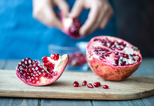 Woman peels pomegranate on wooden table.