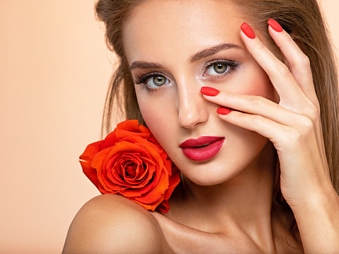 Beautiful young woman with a red flower and nails near face. Art portrait of an attractive model. Girl with bright fashion makeup