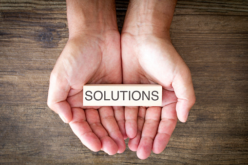 Solutions written on a small wooden block, held in a man's hands. 
Shot from above on a wooden background.