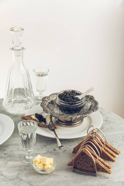 istock Black caviar on ice in silver bowl, Vodka and bread on white marble table 1312686768