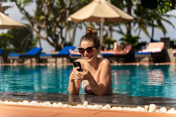 Photo of millennial woman using the phone on the poolside. picture from the back