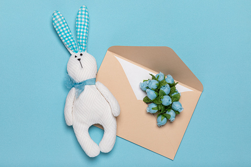 Toy white rabbit hare handmade and paper envelope with delicate flowers flat lay. Concept of spring and romance of letters and cards for holidays.