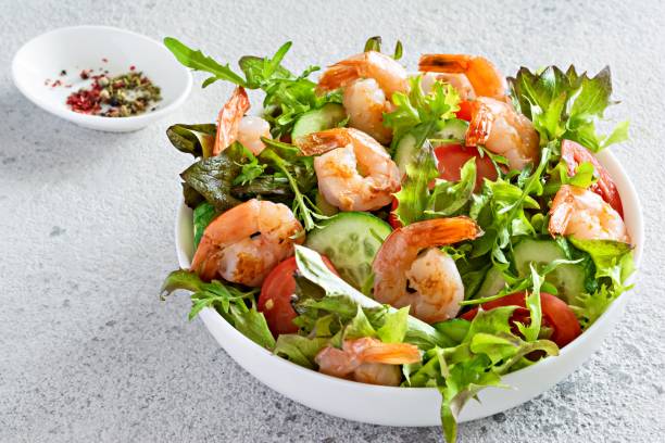 Fresh crispy salad with vegetables and seafood (shrimps) in a white plate on a light background. Fresh crispy salad with vegetables and seafood (shrimps) in a white plate on a light background. Healthy food concept. Shrimp stock pictures, royalty-free photos & images