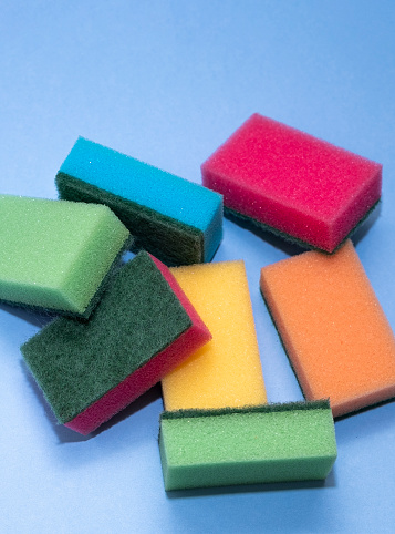 Red, green, yellow, orange and blue dishwashing sponge. Heap, dishwashing sponges on a blue background, copy space.