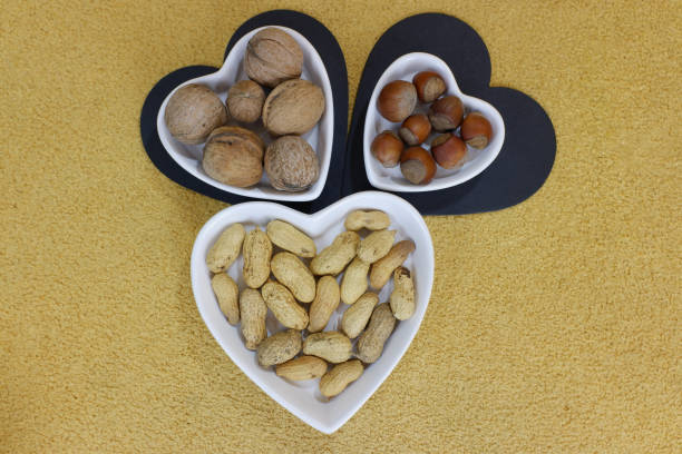 peanuts, hazelnuts, walnuts in heart-shaped plates, on a yellow background. festive romantic dinner. Food background