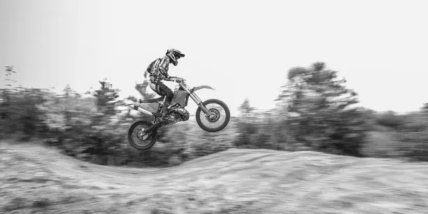 Male portrait of motocross enduro rider outdoors. Sports concept for motorsport on sports track. Professional biker with helmet and stunt motorcycle. Black and white photo