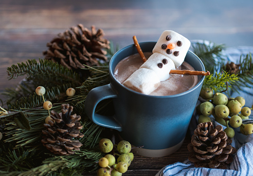 Marshmallow snowman in a mug of hot chocolate with winter decor.