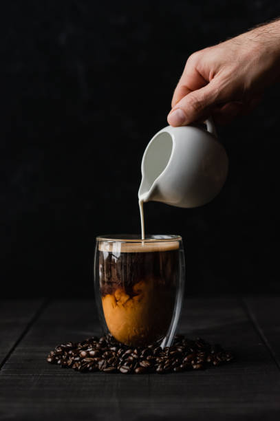 verter crema a mano en una taza de café de cristal transparente sobre fondo negro. - barware fotografías e imágenes de stock