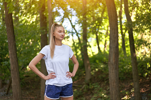 Woman runner standing before exercising summer park morning Middle age athletic female warming up body before running Caucasian person warm up jogging Dressed white shirt shorts running track