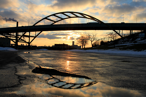 Puente de hone reflejado en charco de agua en el pavimento con la puesta de sol detrás photo