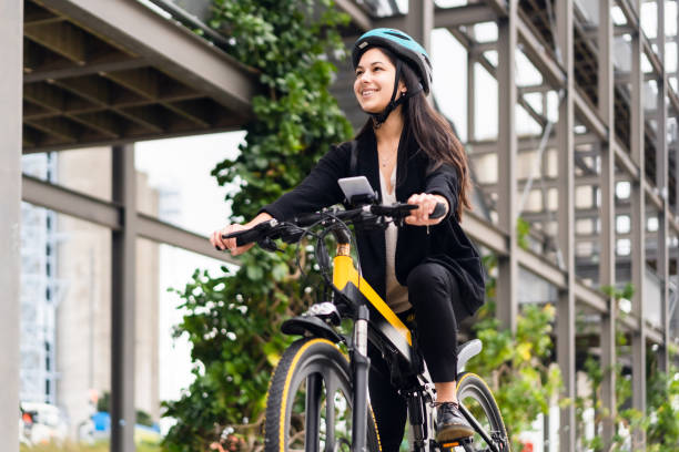Riding Electric Bicycle To Work. Young Eurasian woman riding electric bike to work. electric bicycle photos stock pictures, royalty-free photos & images