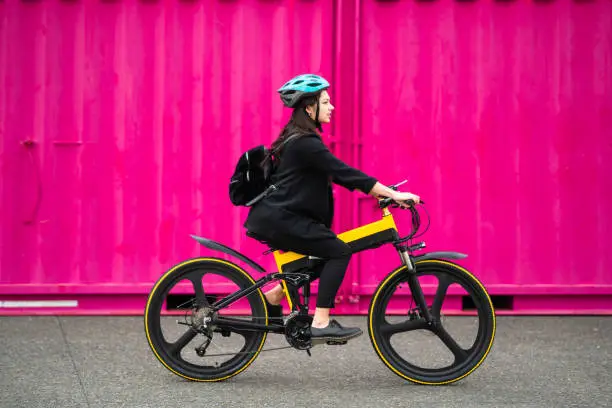 Young woman riding electric bike with pink background.