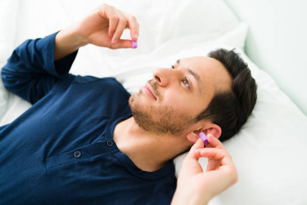 Handsome man using ear plugs to avoid the noise Attractive man in his 30s putting on earplugs before sleeping again because of a noisy morning and neighbors ear plug stock pictures, royalty-free photos & images