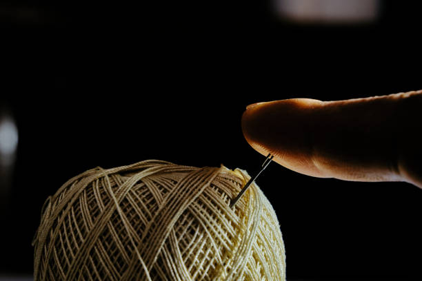 istock A finger pressing on the needle attached in the yellow thread bundle. 1312736606