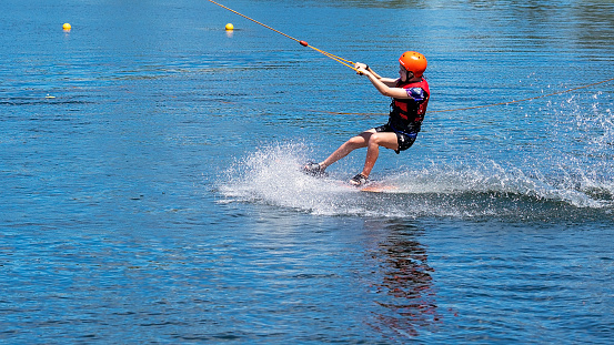 Mackay, Queensland, Australia - April 2021: A young girl wearing a safety helmet and life jacket wake boarding at a cable ski park