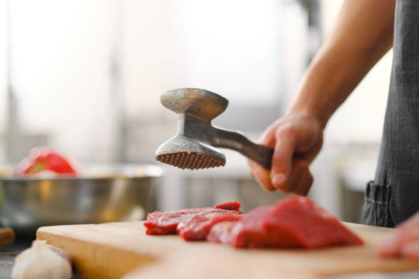 szef kuchni bije kawałek mięsa metalowym młotkiem. gotowanie entrecote lub stek. kucharz w kuchni w restauracji. - mallet zdjęcia i obrazy z banku zdjęć