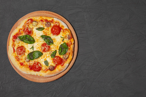 Pizza on wooden plate on black stone background. Cheese pizza with tomato, mozzarella and basil. Close-up photo. Copy space. High quality photo
