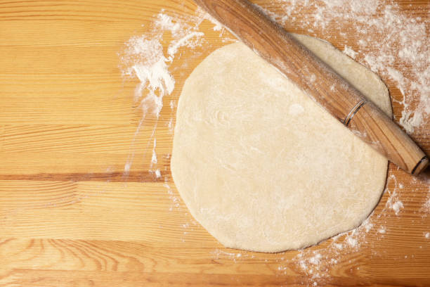 istock Pizza dough on wooden background. Rolling-pin and flour. Selective focus, top view. 1312750908