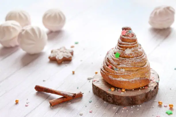 homemade sweet dessert cinnamon roll as an alternative Christmas or new year tree with marshmallow, cinnamon sticks on white wooden background