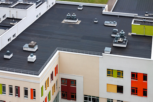 Top view flat roof with air conditioners and hydro insulation membranes on top of a modern apartment yellow green red building.